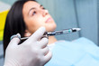 © karelnoppe - Hand holding dental syringe with patient in background.