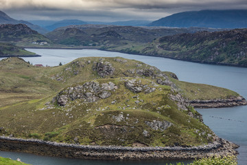 Northwest Coast, Scotland - June 6, 2012: Aerial view over green rocky land tongue protruding into Loch Inchard blue waters. Horizon of mountains and dark clouds.