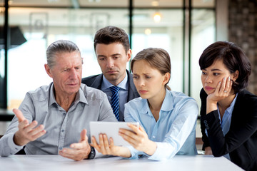 Sad business team looking at touchpad in meeting