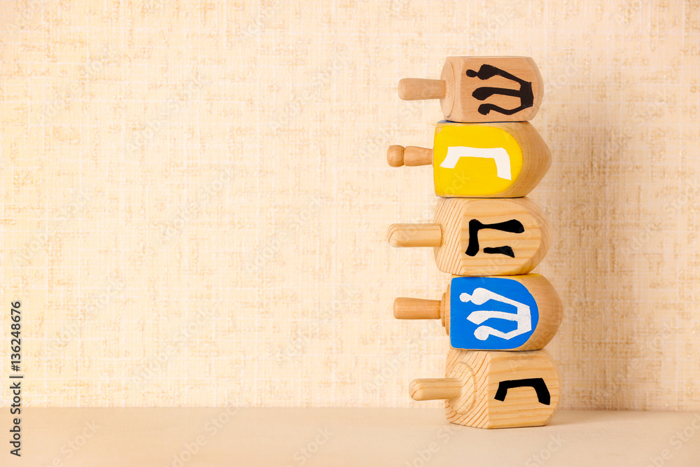 Dreidels for Hanukkah on light table against textured wall