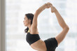 © fizkes - Portrait of young attractive woman practicing yoga, doing Natarajasana exercise, Lord of the Dance pose, working out wearing sportswear, black tank top, shorts, indoor, floor window with city, closeup