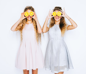 Fashion and beauty. Two stunning beauties girls having fun with slices of oranges closing by them eyes.