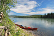 © Nina - Tied up and abandoned red canoe lying on the river bank of the Yukon River in Canada