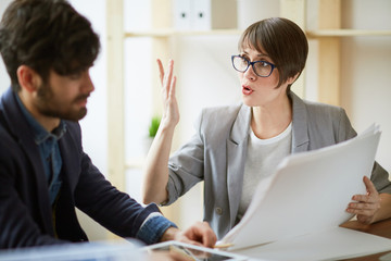 Portrait of two successful business people communicating in office, energetic woman gesturing actively while explaining work plans and documentation details to colleague