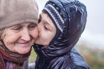 Grandson kisses his grandmother. Older woman and little boy close-up