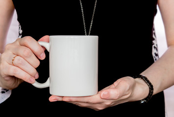 Girl in black dress is holding white cup in hands.