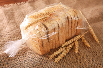 Wall Mural - Sliced bread in plastic bag on sackcloth with wheat spikes closeup