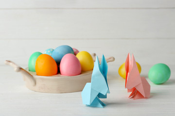 Wall Mural - Easter bunnies with colorful eggs on wooden table against light background