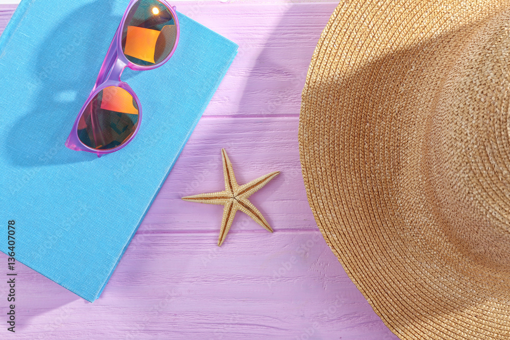 Book, sunglasses and hat on pink wooden table
