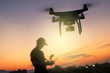 Man playing with the drone by remote control. Silhouette against the sunset sky