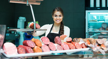 Female Butcher With Wurst And Bologna In Meat Store Counter