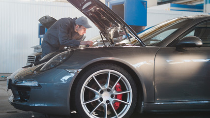 mechanic male in automobile garage checking hood of the luxury sportcar, telephoto