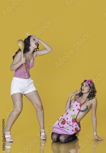 Fotografía Couple of young woman dressed in pin-up style: one standing and holding wooden spoon