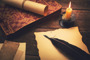 vintage feather with paper and old book on table in light of can