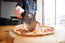Closeup Hand Of Chef Baker In Uniform Blue Apron Cutting Pizza At Kitchen