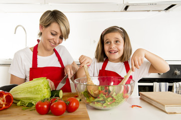 mother and little daughter cooking together with cook  apron preparing salad at home kitchen