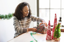 Woman Wrapping Christmas Present While Sitting At Home