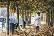 Woman Wearing Coat Walking On Footpath In Park During Autumn