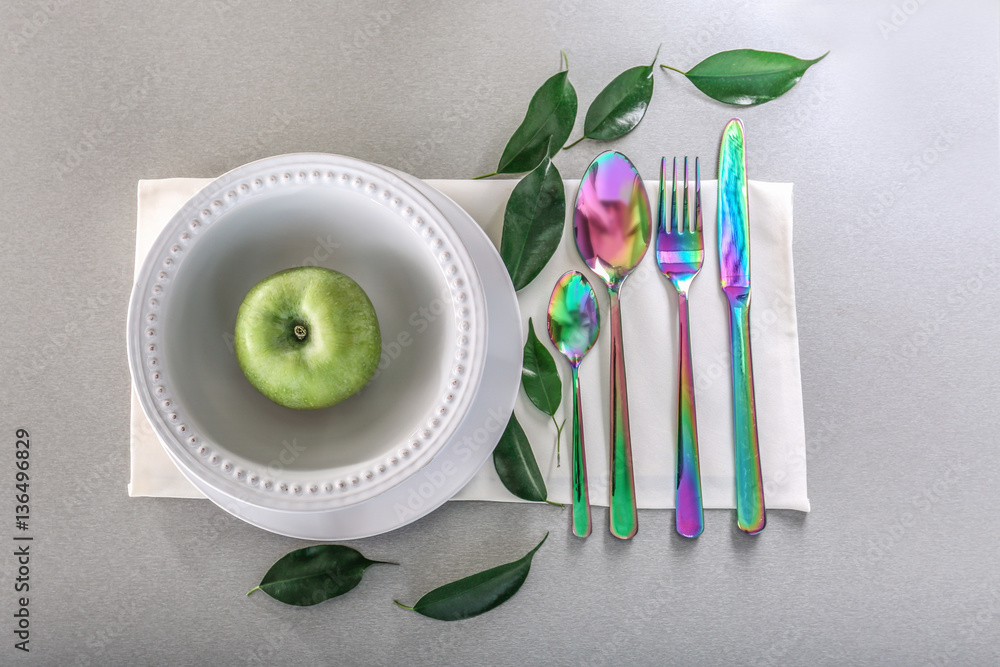 Cutlery set with plates and green apple on gray background