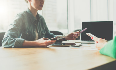 Wall Mural - Teamwork.Two young business woman sitting in meeting room at table and discussing business plan.Girls using smartphones.On table is laptop,tablet PC,paper charts. Online marketing. Students learning.