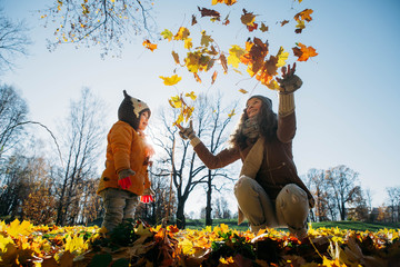 mother throws autumn leaves on daughter in the park