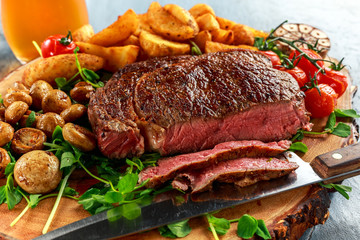 Cooked Beef Ribeye Steak with Potato, Mushrooms, tomatoes on wooden board.