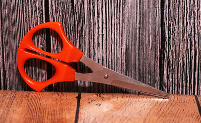 Scissors with orange handle on a wooden background