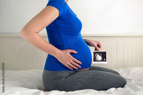 Plakat kobieta w ciąży siedzi na białym łóżku i trzyma dziecko USG