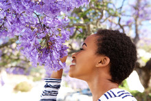 Young Black Woman Smelling Flowers On Tree