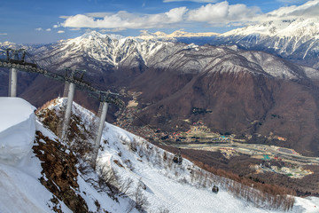 Wall Mural - Scenic landscape of cable way ski lift in Gorky Gorod mountain ski resort and the river valley at early spring. Beautiful sunny scenery with snowy forest and peaks. Sochi, Russia