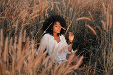 Attractive Young African American Woman Sitting On Field At Sunset