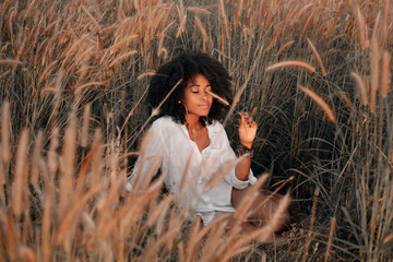 attractive young african american woman sitting on field at sunset