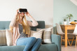 © andreaobzerova - Attractive woman wearing virtual reality glasses lying on a couch. Virtual reality headset. Lifestyle virtual reality concept.