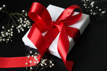 Gift in a white package tied a red ribbon on a black background.