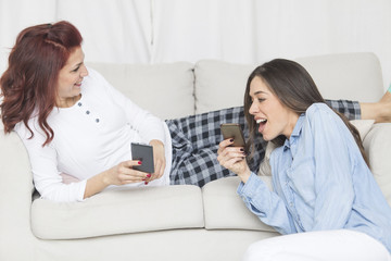 Wall Mural - Two happy young female friends having fun together using smartphone