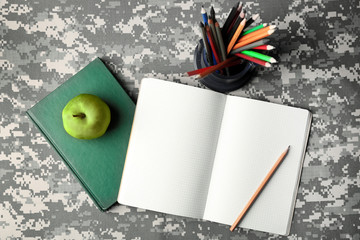 Poster - Apple and stationery on camouflage background. Military education concept