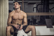 © theartofphoto - Muscular, shirtless young man resting in gym during workout, showing muscular torso, pecs and abs, holding a towel in his hands, sitting on bench