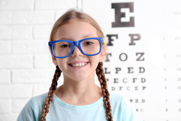 Wall Mural - Little girl with spectacles on ophthalmic test chart background