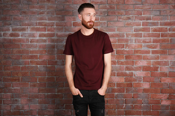 Wall Mural - Young handsome man in claret red T-shirt on brick wall background