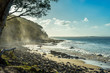 Tropical Surfer Beach. Idyllic sunset at famous Tea Tree Bay, Noosa, Australia. Sun shining through spray mist in the eucalyptus trees. Tropical stone pebbles in the foreground. Two surfers ret