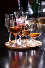 Glasses Of Different Shapes With Different Alcohol On A Wooden Round Board On The Bar