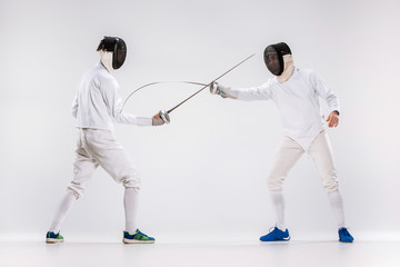 The two men wearing fencing suit practicing with sword against gray