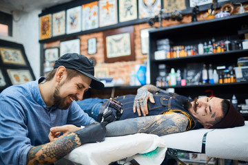 Wall Mural - Happy young tattooer in ball-cap working with client