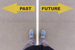 Past and future text arrows on asphalt ground, feet and shoes on
