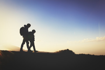 silhouettes of father and son hiking at sunset