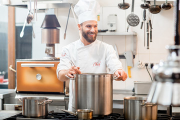 Chef cook in uniform cooking soup in the big cooker at the restaurant kitchen