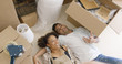 Attractive mixed race couple lying on the floor among unpacked boxes in their new home they just moved in. Talking about future and smiling.