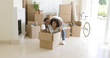 © Dash - Fun young African woman with an afro hairstyle sitting inside a packing box with her laughing husband behind her as they move into a new home with a stack of packed cartons.