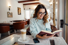 Young  Beautiful Woman In Glasses Reading Interesting Book In Cafe