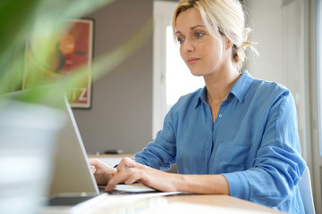 Wall Mural - Portrait of blond woman with blue shirt working from home on laptop